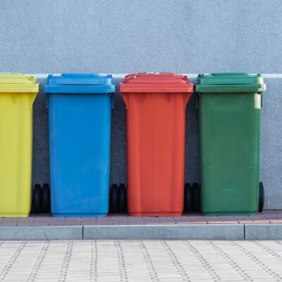 A row of multicolored recycling bins against a gray wall.