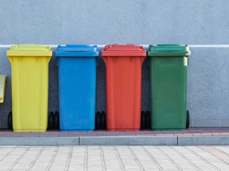 A row of multicolored recycling bins against a gray wall.