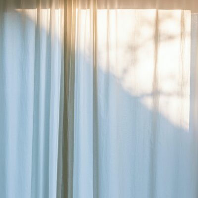 Sun shines through a window covered by gauzy white curtains.